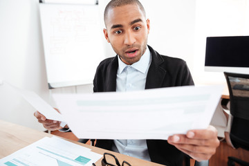 Shocked businessman looking at paper and holding eyeglasses