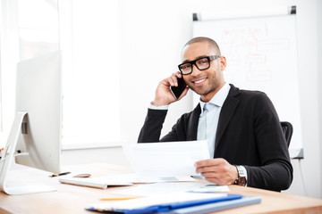 Happy smiling businessman holding documents and talking on mobile phone