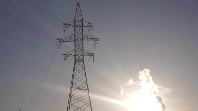 Electric power transmission line support and smoking stack against sunset sky