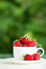 Strawberries in a white Cup on green background.