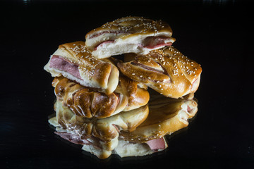 Булочка с запечённой колбасой на тёмном фоне.