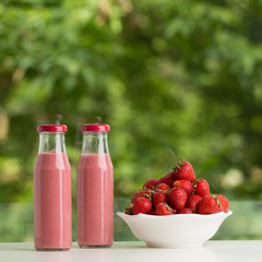 Strawberry smoothie in glass bottle on green background.