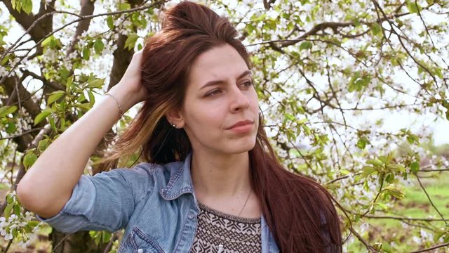 Beautiful young woman fix her hair near blooming tree. Close up. Slow motion