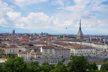 Obraz premium Cityscape of Torino (Turin, Italy) with the Mole Antonelliana and the hot-air baloon towering over the buildings. Wind storm clouds over the Alps in the background.