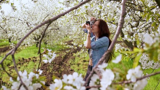Beautiful young woman taking photos with old film camera of blooming tree. Close up. Slow motion