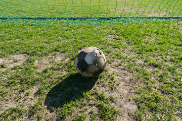 Old ragged soccer ball on grass in front of gate.