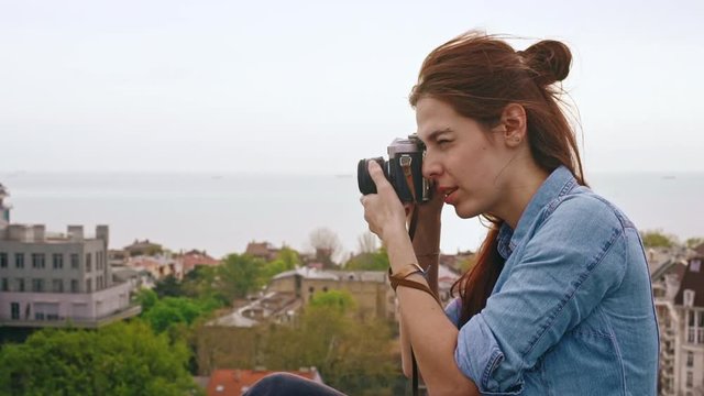 Beautiful young female photographer take photos of cityscape from the roof.  Slow motion