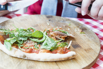 Italian pizza with ham and arugula on wooden plate. Pizza is partially eaten.