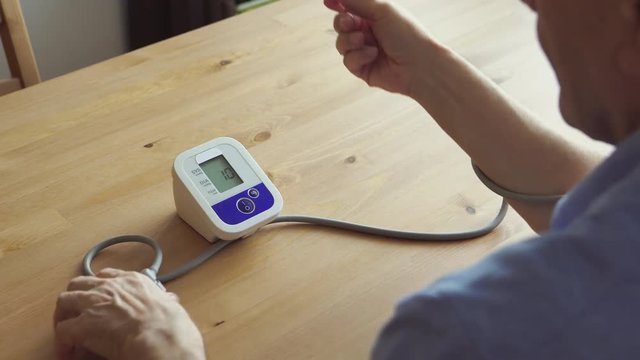 BACK VIEW: An elderly man measuring the blood pressure at home - Powered by Adobe