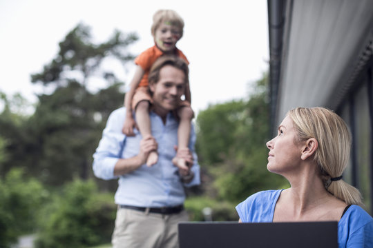 Woman looking at family while using laptop in yard