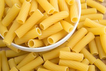 Bowl filled with rigatoni pasta with more pasta spilled onto a cutting board.