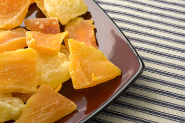 Plate of sugared pineapple, mango and papaya on a blue striped tablecloth at an angle.