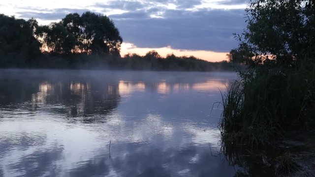 morning sunrise reflection in misty fog rise from flowing river water.