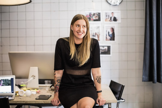 Smiling young businesswoman leaning at table in new office