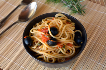 Spaghetti a la puttanesca on a brown bowl. Italian food.
