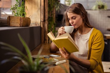 Casual woman reading a book while drinking - obrazy, fototapety, plakaty