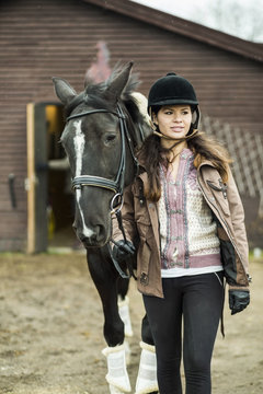Young woman with horse walking outside barn