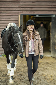 Young woman with horse walking outside barn with man in background