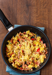 scrambled eggs with ham, vegetables and cheese in a frying pan on wooden table
