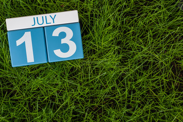 July 13th. Image of july 13 wooden color calendar on greengrass lawn background. Summer day, empty...