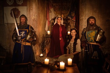 Medieval queen with her courtier and knights on guard in ancient castle interior.