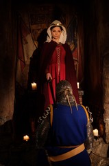Medieval queen doing knighting ceremony in ancient castle interior.