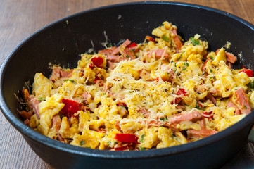 scrambled eggs with ham, vegetables and cheese in a frying pan on wooden table