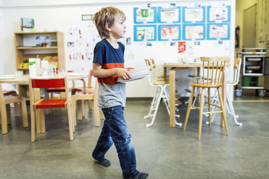 Boy carrying stack of plates in kindergarten 