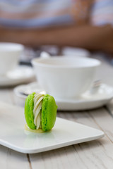 Green macaron with cup of tea in background