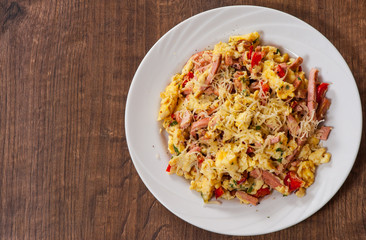 scrambled eggs with ham, vegetables and cheese in a plate on wooden table