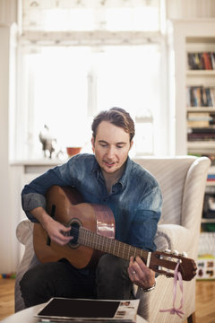 Mid adult man playing guitar at home