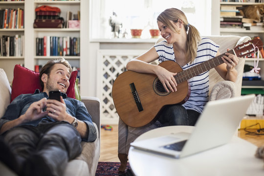 Happy woman playing guitar for man at home