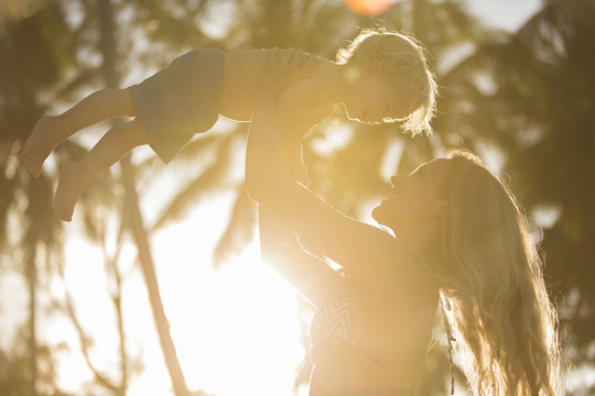 Happy mother lifting up her son in backlight