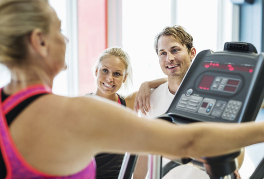 Friends looking at woman exercising on treadmill at gym