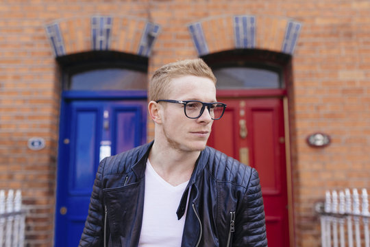 Portrait of young man wearing black glasses in front of a brick house