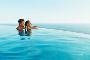 Couple In Love At Luxury Resort On Romantic Summer Vacation. People Relaxing Together In Edge Swimming Pool Water, Enjoying Beautiful Sea View. Happy Lovers On Honeymoon Travel. Relationship, Romance
