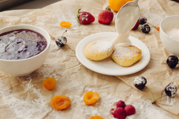 Cheese pancakes with sour cream in spoon. Parchment background