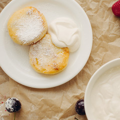 Cheese pancakes with sour cream on parchment background