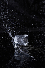 Naklejka na ściany i meble Ice cube flying with splashes on a black background