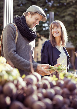 Young couple buying fresh vegetables at outdoor market 