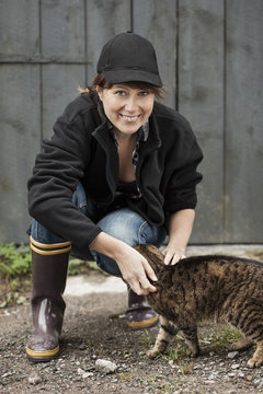 Full length portrait of female farmer petting cat against barn
