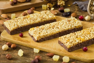 Energy granola bars with cornflakes, puffed cereals and rolled oats covered in chocolate on wooden cutting board