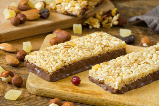 Granola bars with cornflakes, puffed cereals and rolled oats covered in chocolate on wooden cutting board
