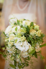 Obraz na płótnie Canvas A shot of a bride from the neck down out of focus holding a white and green bouquet of flowers.