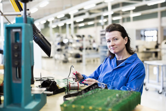 Portrait of confident female technician working on circuit board at desk in industry