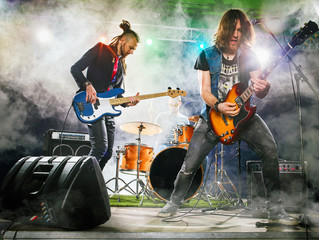Rock band performs on stage. Guitarist, bass guitar and drums. The guitarist plays solo.