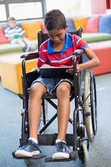 Fototapeta na wymiar Disabled schoolboy on wheelchair using digital tablet in library