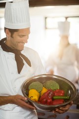 Smiling chef showing bowl of vegetable 