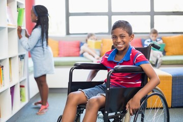 Portrait of disabled schoolboy on wheelchair in library