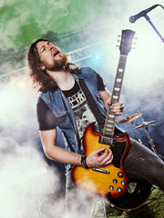 Rock band performs on stage. Guitarist, bass guitar and drums. The guitarist plays solo.